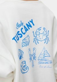 Sudadera blanca con estampados gráficos en azul de conchas, cangrejo, langosta, velero y texto "Italia TOSCANA" y "Mar de Amor". Textura suave.