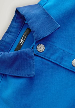 Blå skjorta med krage tillverkad av texturerat tyg. Har knappstängning med metallsmycken och en etikett som visar märket 'NEXT'.