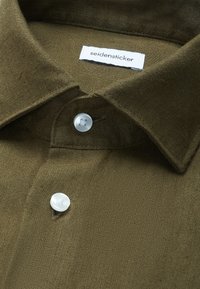 Gros plan sur une chemise col olive avec des boutons blancs et une étiquette blanche "seidensticker" à l'intérieur du col.