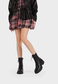 Botas de cuero negro con cordones hasta el tobillo, con una suela gruesa y superficie texturizada, que presentan un caña alta y cordones resistentes.
