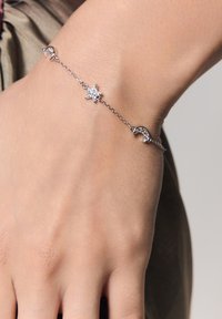 Srebrna bransoletka z łańcuszka z centralnym wzorem w kształcie gwiazdy i dwoma akcentami w formie półksiężyca, ozdobiona przejrzystymi kamieniami dla blasku.