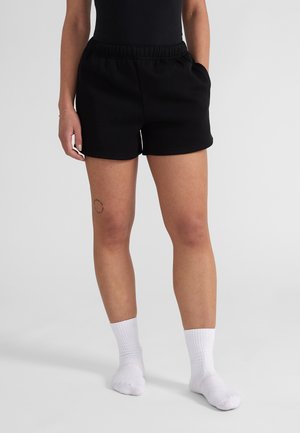 Zwarte katoenen shorts met een elastische tailleband en zijzakken, gecombineerd met witte, geribbelde crew-sokken, die een gladde textuur tonen.