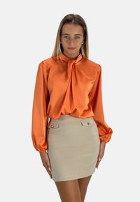 Oranje satijnen blouse met een gestrikte halslijn en puffmouwen, gecombineerd met een beige kokerrok met twee decoratieve knopen.
