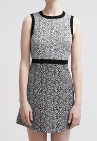 Svart och vit ärmlös klänning med ett mönstrat överdel som har utsmyckade mönster och ett solidt svart midjebälte. Skater-siluett.