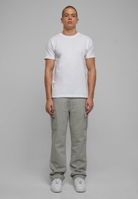 Witte T-shirt met korte mouwen, gecombineerd met lichtgrijze cargo sweatpants met zijzakken en witte sportschoenen.