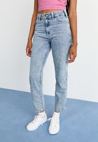 Lyseblå høy midje jeans laget av denim, med en falmet tekstur og klassisk fem-lomme-design, paret med hvite joggesko.