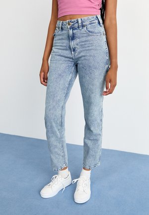 Jeans a vita alta di colore blu chiaro realizzati in denim, con una texture scolorita e un classico design a cinque tasche, abbinati a sneaker bianche.