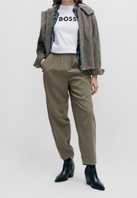 Khaki byxor med sidofickor, grå mockajacka, vit t-shirt med svart text "BOSS" och svarta klackboots.