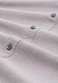 Tissu texturé rose clair avec un petit motif répétitif. Comprend des boutons noirs sur les bords gauche et droit.