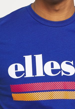 Persona che indossa una maglietta blu con la scritta bianca "elles" e due barre a strisce in rosso e arancione sotto il testo, primo piano sul petto e sul collo.