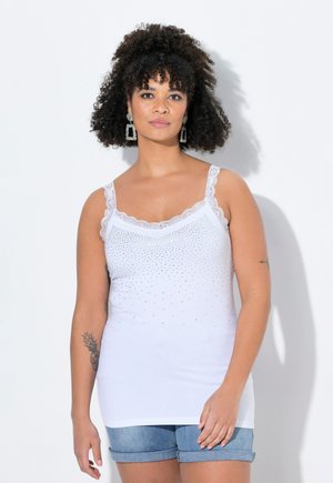 Top bianco con pizzo e dettagli in strass, con spalline sottili e silhouette aderente, abbinato a pantaloni di jeans corti.