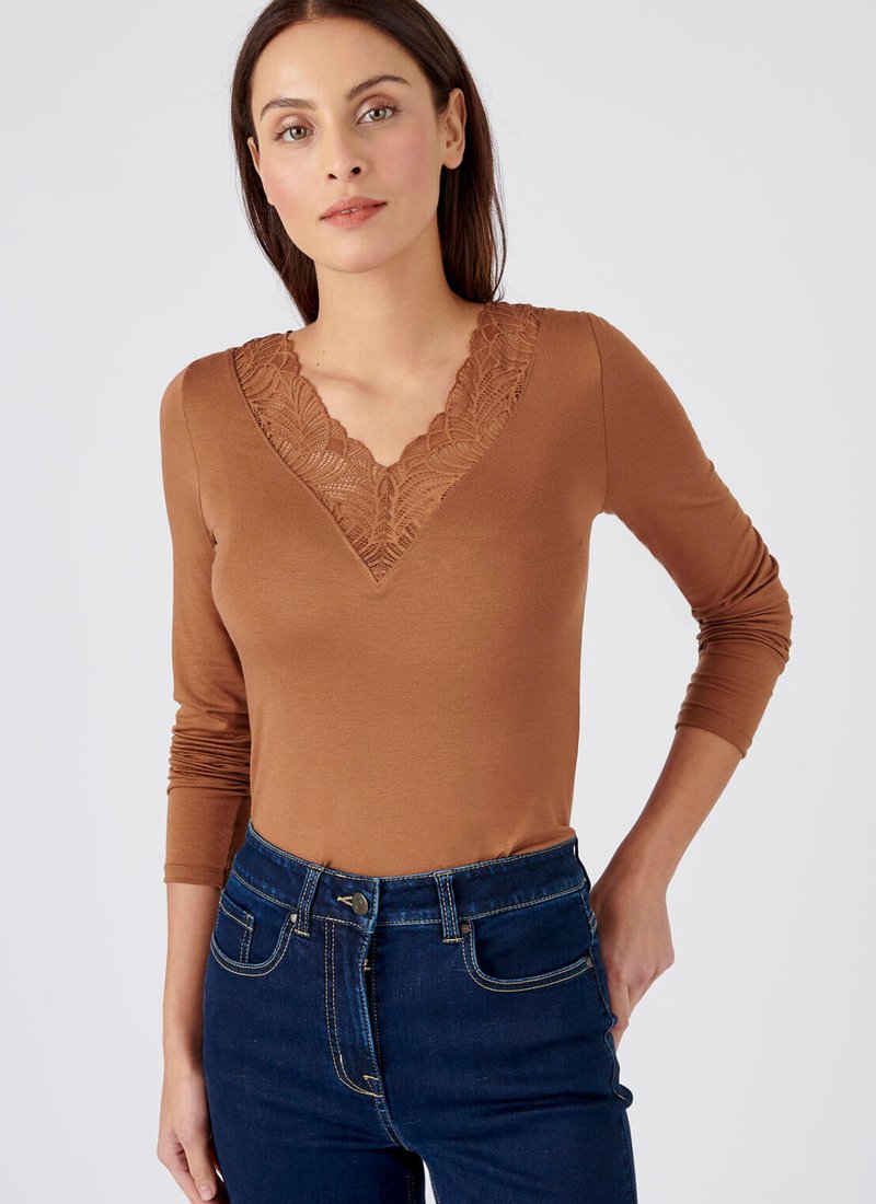 Top lungo marrone con maniche a lunghe e scollatura a V decorata con pizzo, abbinato a jeans scuri a vita alta, che mostrano una texture liscia e una forma aderente.