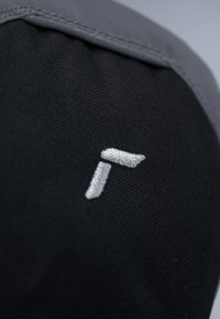 Schwarzer Stoff mit grauen Akzenten, der ein eingesticktes silbernes Logo zeigt. Die Textur ist glatt mit einem leicht gewebten Muster.