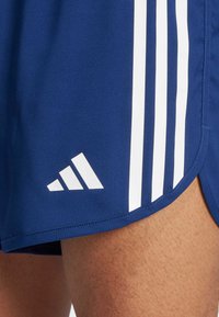 Granatowe szorty sportowe z trzema białymi pionowymi paskami, z białym logo Adidasa na krawędzi. Wykonane z teksturowanej tkaniny poliestrowej.