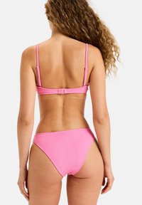 Roza bikini komplet z teksturiranim dizajnom, tankimi nastavljivimi naramnicami in zaponko na hrbtni strani zgornjega dela. Spodnji del ima usklajen stil.
