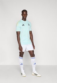 Light blue short-sleeve jersey with black logo and accents, paired with white shorts and socks featuring blue stripes. White cleats.