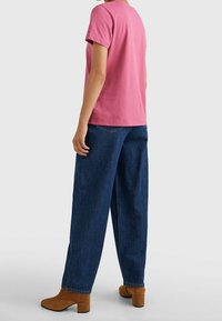 Rosa bomullströja i kombination med löst sittande mörkblå jeans och tanfärgade höga stövlar. Tröjan har korta ärmar och rund halsringning.