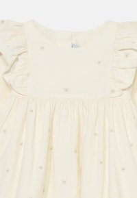 Rochie crem deschis cu mâneci volănașe și broderie în formă de stea, aurie. Material moale, cu talie strânsă și decolteu rotund.
