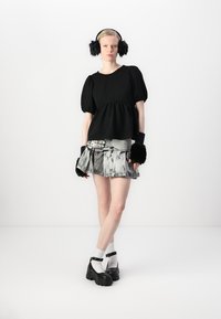 Top nero con maniche a sbuffo e dettaglio peplum, abbinato a una gonna grigia con un motivo marmorizzato e orlo frangiato. Scarpe chunky nere e cuffie.