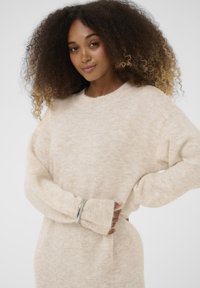 Svetlosmeđi pleteni pulover s opuštenim krojem, dugim rukavima, rebrastim manžetama i mekanom teksturom. Sadrži suptilan uzorak kroz cijeli proizvod.