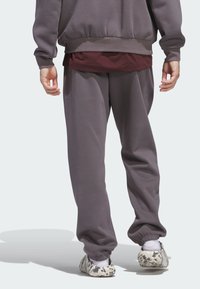 Grauer Kapuzenpullover und passende Jogginghose mit entspannter Passform, ausgestattet mit elastischen Bündchen. Darüber getragen ein weinrotes Shirt. Einzigartige gemusterte Schuhe.