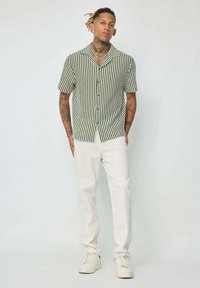 Chemise à manches courtes avec des rayures verticales vertes et blanches, associée à un pantalon blanc et des baskets blanches. Comprend un col et une poche poitrine.
