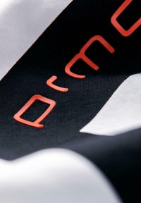 Černobílá látka s červeným raženým písmem. Materiál se zdá být hladký s mírným leskem a má jemnou texturu.
