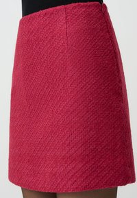 Red woven mini skirt with a textured fabric. Features a straight silhouette and stitched detailing along the waist.