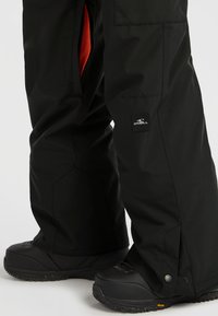 Zwarte sneeuwbroek met een mesh voering, ritssluitingen en logo patch. Gecombineerd met zwarte, gestructureerde sneeuwlaarzen met een robuuste zool.