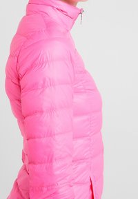 Rosa puffjacka med hög krage, med kviltade sektioner och dragkedjestängning. Tillverkad av ett slätt, lätt material.