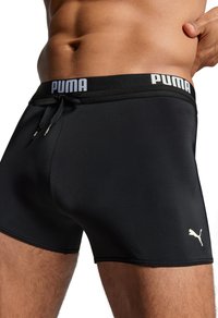Schwarze Sportsch shorts mit strukturierter Oberfläche, ausgestattet mit einem Kordelzugbund und einem weißen Logo. Das Design ist figurbetont mit minimalen Nähten.