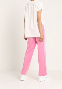 Camiseta blanca de manga corta combinada con pantalones de chándal rosas con rayas laterales blancas y zapatillas gruesas blancas, mostrando un ajuste relajado.