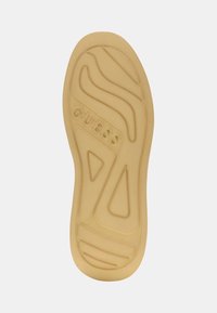 Suola in gomma beige con pattern testurizzati e logo "GUESS". Presenta scanalature per la trazione e un design ergonomico.