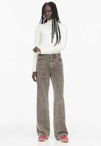 Pulover alb cu guler înalt, blugi largi de culoare olive estompată cu nervuri verticale, adidași roz și negri cu talpă bej. Elemente de design simple.