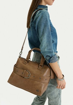 Donna che indossa una camicia di denim e jeans chiari, con una grande borsa a tracolla in pelle marrone con dettaglio fibbia.