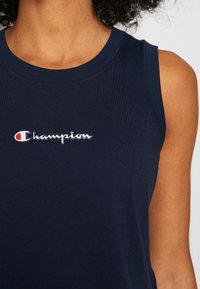 Granatowy bawełniany tank top bez rękawów z haftowanym na środku białym i czerwonym logo "Champion". Gładka tekstura.