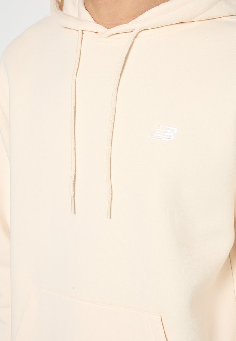 Sweat-shirt couleur pêche en tissu doux, avec une poche kangourou, une capuche à cordon de serrage réglable, et un petit logo blanc sur la poitrine.