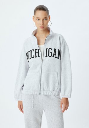 Graue Zip-Jacke aus weichem Material mit schwarzer "MICHIGAN"-Beschriftung auf der Brust, mit elastischen Bündchen und seitlichen Taschen.