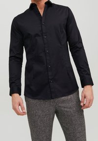 Svart långärmad skjorta med knappstängning fram, gjord av ett mjukt tyg. Har en klassisk krage och en slim fit. Inga synliga mönster.