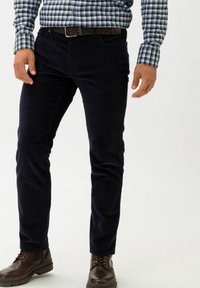 Navynäby byxor med slim fit, som har sidofickor och en texturerad tyg. Bärs med en rutig blå skjorta och bruna snörboots.