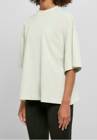 Světle zelené oversized tričko s krátkými rukávy, kulatým výstřihem a jemnou texturou. Navrženo pro volný střih s rovnou dolní částí.