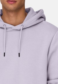 Lichte lavendel hoodie met een kangoeroezak, verstelbare koordjes en zwarte rubberen uiteinden. Zachte textuur en ontspannen pasvorm ontwerp.