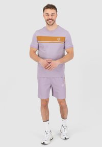 Lichtpaarse sportshirt met een oranje horizontale streep, gecombineerd met bijpassende shorts. Bevat een logo op de borst en zijkant van de shorts.