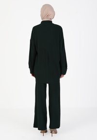 Set in maglia a coste di un verde scuro, composto da un tunica lunga con un colletto alto e pantaloni a gamba larga, progettato con una silhouette morbida e una texture piacevole.