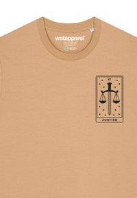 Tan katoen t-shirt met een zwarte afbeelding van schalen en een zwaard binnen een rechthoekige rand, met de tekst "JUSTITIE" onderaan.