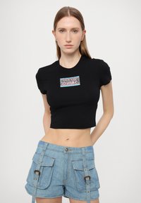 Melnā īsā T-kreklā ar īsām piedurknēm ir krāsaina grafika centrā. Pāris veido ar gaiši ziliem denim šortiem ar kabatām.