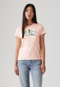 T-shirt en coton rose clair avec un graphique floral et le texte "Levi's" en blanc. Manches courtes et décolleté rond. Coupe décontractée.