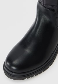Black leather boot with a smooth finish, rounded toe, and thick textured rubber sole. Features a padded shaft without visible hardware.