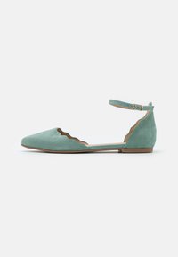 Zapatos planos de ante en verde menta con punta afilada, bordes con volutas y correa ajustable en el tobillo. Suela y forro en marrón.