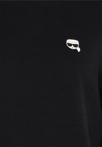 Svart bomullströja med en liten vit tecknad figur med solglasögon som accentdetalj på vänster bröstområde.